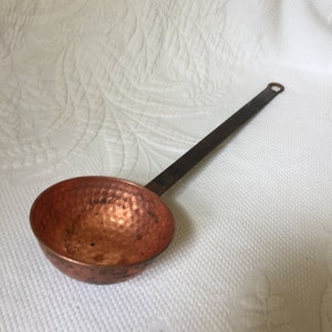 May include: A copper ladle with a hammered finish and a long, dark brown wooden handle.