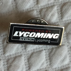 May include: A black and silver pin with the text "Powered by Lycoming Textron Lycoming" in white letters.