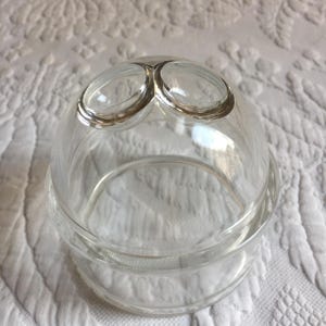 May include: A clear glass double-tiered dome with a silver rim. The top tier has two circular openings.