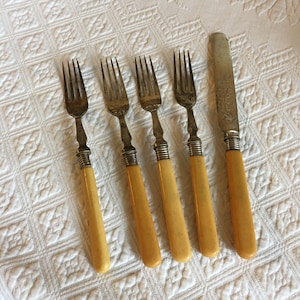 Puede incluir: Conjunto de cinco tenedores de plata y un cuchillo con mangos de color marfil. Los tenedores y el cuchillo tienen diseños ornamentados.