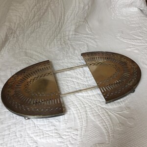 May include: A silver-plated, two-piece, decorative serving tray with a scalloped edge and an intricate, openwork design. The tray is made of two half-circles that are connected by two metal rods.