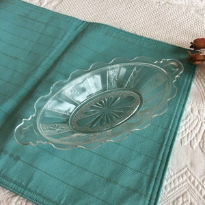 May include: A clear glass oval serving dish with a scalloped edge and two handles. The dish has a decorative, embossed pattern.