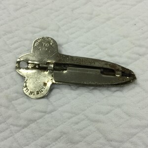 May include: A vintage, silver-colored can opener with a folding design. The opener has a clover-shaped handle with the text "TURN SLOWLY TO RIGHT" and "MADE IN USA". The blade section is elongated with the text "ALLEN'S FOLDING".