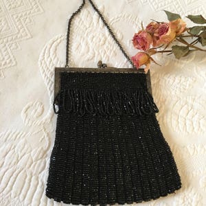 May include: A black beaded evening bag with a silver chain strap and a clasp closure. The bag is made of small black beads and has a fringed design.