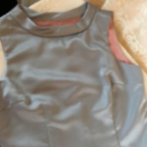 May include: A sleeveless, light gray satin dress with a high neckline.