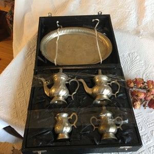 May include: A silver tea set in a black velvet lined box. The set includes a tray, two teapots, and two creamer pitchers.