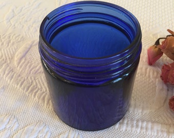 May include: A cobalt blue glass jar with a wide mouth opening. The jar has a smooth, rounded shape and a glossy finish.
