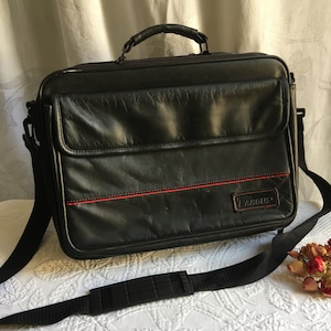 Sac de nuit Targus en vinyle noir. Pochettes extérieures, fermeture éclair et fermeture Velcro. Attache rembourrée pour ordinateur, séparations, etc.