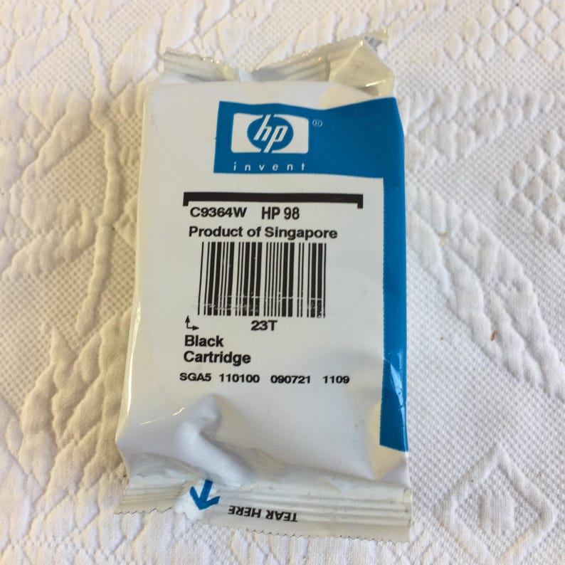May include: A white and blue HP 98 black ink cartridge in its original sealed plastic packaging. The label displays the HP logo, model number C9364W, a barcode, the text Product of Singapore, and the words Black Cartridge with a tear here indicator.