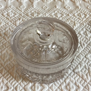 Könnte beinhalten: Ein klares Glasgefäß mit Deckel und einem Knopf oben. Das Gefäß hat ein strukturiertes Muster an den Seiten.