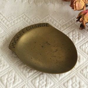 Puede incluir: Un pequeño plato ovalado de latón con las palabras "Pocket Change" grabadas en el borde.