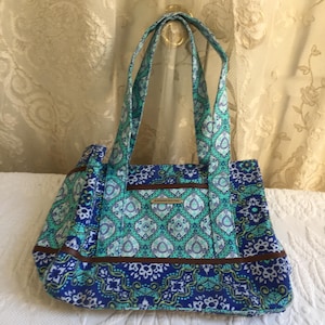 Bolso de mano de tela azul, aguamarina, verde y blanca de Raymond Waites con detalles de vinilo marrón. Asas superiores con cierre a presión para agrandar, cierre superior y bolsillos.