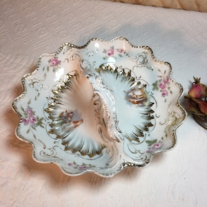 May include: A white porcelain divided serving dish with a scalloped edge. The dish has a gold rim and floral design with pink roses. The centre of the dish has a handle and two separate bowls.