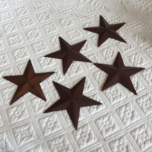 May include: Five brown metal star-shaped ornaments on a white textured surface.