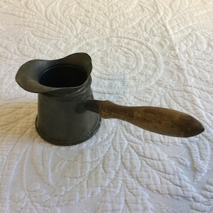 May include: A vintage metal coffee pot with a wooden handle. The pot is dark gray and has a rounded shape. The handle is brown and has a slightly curved shape.