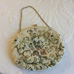 Monedero de cuentas hecho a mano con diseño de tapiz y asa de cadena tipo serpiente. Forro de seda blanca. Cuentas blancas que acentúan el diseño del tapiz. Bolsillo interior.