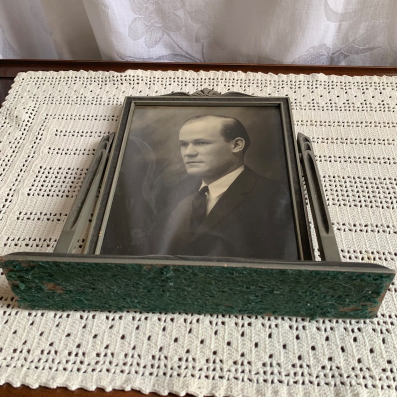 May include: A silver-toned picture frame with a black and white photo of a man wearing a suit and tie. The frame has a green felt backing.