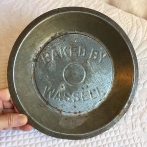 Vintage Baked by Wassell Pie Plate. Metal Pie Plate With Molded Name. Vent Holes in Bottom. Dark with Age and Use Plate.