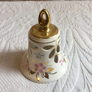 May include: White porcelain bell with a gold-painted top and floral design. The bell has cut-out designs and the text "The Sàndor Collection Made in Hungary" is printed on the side.