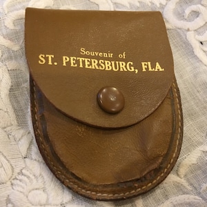 May include: A brown leather coin purse with a gold inscription that reads "Souvenir of ST. PETERSBURG, FLA."