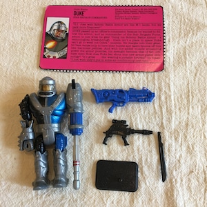 Vintage 1992 GI Joe Duke Star Brigade Commander actionfigur. Hasbro, Inc. Rörlig docka. Skjutmaskin, missil, hjälm, 2 pistoler, kniv, stativ.