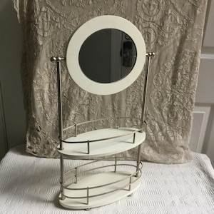 Tabletop Mirror with Shelves to Hold Makeup. Mirror Flips to No Mirror. White with Silver Metal. Ball Feet on the Bottom.