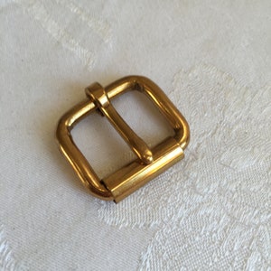 May include: A gold-toned metal buckle for a belt or strap.
