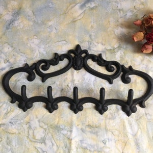 May include: Black cast iron wall mounted coat rack with five hooks and a decorative scroll design.