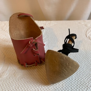 May include: A wooden spinning top with a leather carrying case. The case is red and has a lace-up closure. The top is brown and has a black string attached to it.