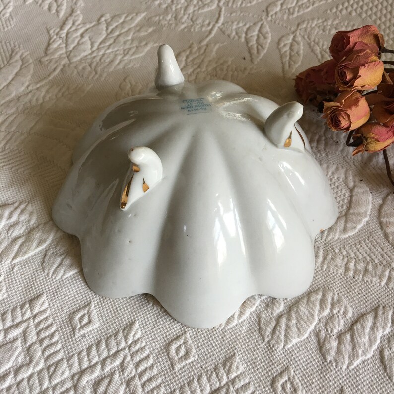 May include: White porcelain bowl with three gold-trimmed feet. The bowl has a scalloped edge and is marked "Made in Japan" on the bottom.