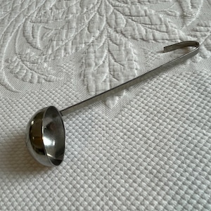 May include: A silver ladle with a long handle. The ladle is made of metal and has a rounded bowl.