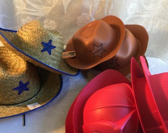 May include: A selection of toy hats: straw cowboy hats with blue stars, brown sheriff hats with a star badge, and red firefighter helmets with an FD logo.