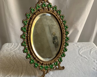 Miroir victorien fantaisie en laiton doré biseauté avec des formes de trèfle peintes en vert. Motif clouté autour du miroir. Support de table à l'arrière.