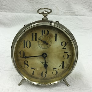 Puede incluir: Un despertador vintage plateado con esfera crema. Tiene grandes números negros, una esfera interior más pequeña y el texto "Westclox Big Ben". El reloj tiene un asa y se apoya en pequeños pies. El diámetro es de aproximadamente 10 cm.