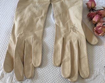 Könnte beinhalten: Ein Paar cremefarbene Lederhandschuhe mit zarter Blumenstickerei. Die Handschuhe sind lang und haben eine spitze Fingerspitze.