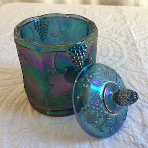 Könnte beinhalten: Eine blaue, irisierende Glasdose mit Deckel, verziert mit einem Traubenranken-Design. Die Dose hat eine sechseckige Form und der Deckel einen Knopf.