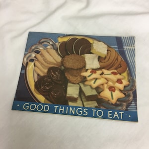 May include: A vintage cookbook cover featuring a colourful illustration of a plate filled with various cookies, cakes, and pastries. The text on the cover reads "GOOD THINGS TO EAT."