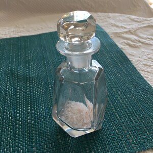 Puede incluir: Una botella de vidrio transparente con un tapón facetado, llena de cristales de sal rosa del Himalaya.