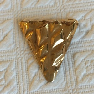 May include: A gold-colored triangular brooch with a textured surface.