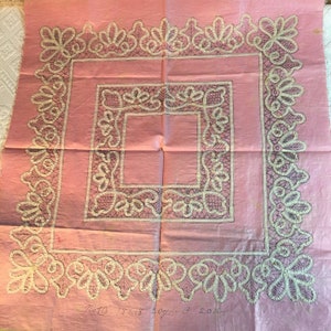 May include: A pink fabric square with a lace pattern printed on it. The lace pattern is in black and white. The fabric is folded in the center. The text "No 13 15/18 20/22 3 20/22" is written in black ink in the bottom right corner.