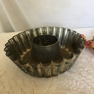 May include: A vintage metal cake pan with a fluted edge and a removable center tube. The pan is silver in color and shows signs of age and use.
