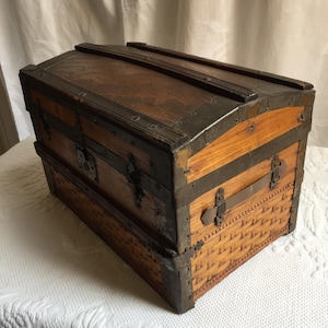 Puede incluir: Un ba&uacute;l de madera antiguo con detalles met&aacute;licos y un patr&oacute;n tejido en la parte inferior. El ba&uacute;l tiene una tapa con bisagras y una cerradura.