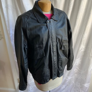 Blouson aviateur ou aviateur en cuir vintage Georgetown Leather Design XLL en cuir. Épaulettes. Doublure en nylon 50/50 et acétate. Mastic poly.