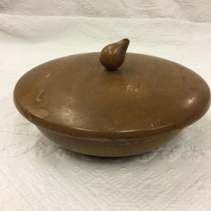 以下が含まれることがあります： 丸い木製のボウルと、それに合う蓋。 蓋には小さな涙型の取っ手が付いています。 ボウルと蓋は温かみのあるミディアムブラウン色で、木目が見え、わずかな欠陥があります。