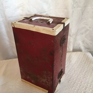 May include: A vintage red rectangular box with a white handle and trim. The box has metal clasps and corner reinforcements. The paint is distressed, giving it a rustic appearance. The box is likely used for storage.