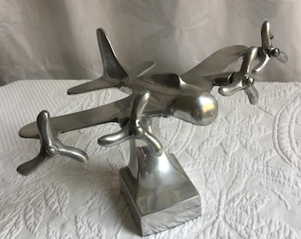 Aeroplano vintage in alluminio argentato su supporto sagomato per esposizione. Non è un giocattolo, ma un oggetto da collezione. Quattro eliche girevoli.