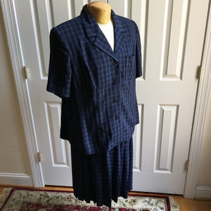 May include: A blue and white plaid skirt suit with a short-sleeved jacket and a pleated skirt.