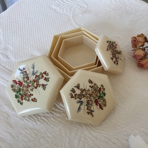 Könnte beinhalten: Ein Satz von vier sechseckigen, ineinander verschachtelten Boxen mit Blumendesigns. Die Boxen sind aus weißem Kunststoff und haben einen cremefarbenen Hintergrund mit roten, grünen und blauen Blumenmustern.