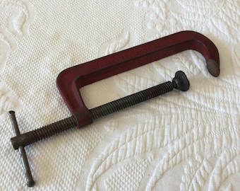 May include: A red metal C clamp with a threaded screw and a T-shaped handle. The clamp is labeled "OLIVER MANUFACTURING CO."