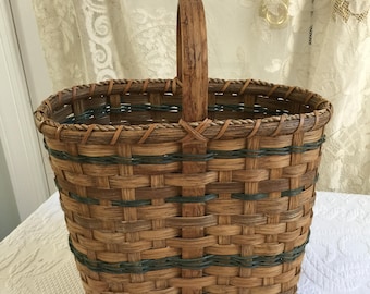 Cesta vintage ancha de mimbre con asa superior estrecha y juncos redondos verdes tejidos como decoración. 5 1/2" x 10 1/2" x 14" de alto.